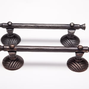 May include: Two black metal towel bars with decorative, textured, round bases. The bars are slightly angled and have a rustic finish.