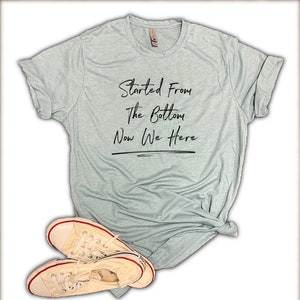 May include: A light blue t-shirt with the text "Started From The Bottom Now We Here" in black lettering.