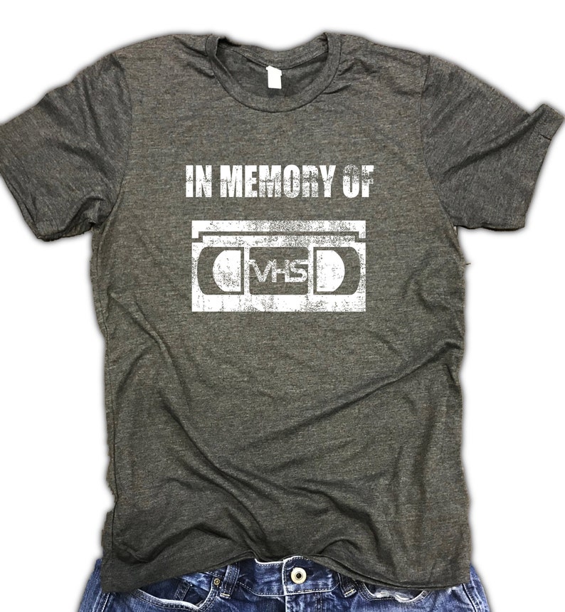 May include: A dark gray t-shirt with a white graphic of a VHS cassette tape and the text "In Memory Of".