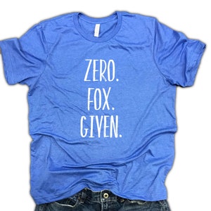 Puede incluir: Una camiseta azul claro con el texto "ZERO. FOX. GIVEN." en blanco. La camiseta est&aacute; hecha de un material suave y est&aacute; doblada sobre unos vaqueros azules. La camiseta tiene cuello redondo.