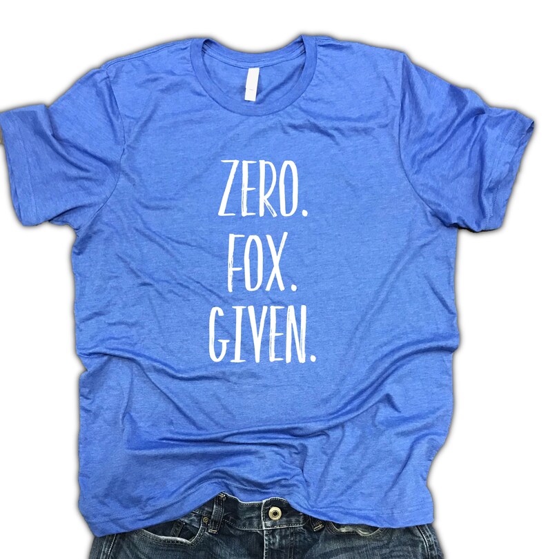 Puede incluir: Una camiseta azul claro con el texto "ZERO. FOX. GIVEN." en blanco. La camiseta est&aacute; hecha de un material suave y est&aacute; doblada sobre unos vaqueros azules. La camiseta tiene cuello redondo.