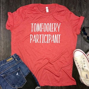 May include: Red t-shirt with white text that reads "TOMFOOLERY PARTICIPANT".