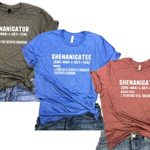 Puede incluir: Tres camisetas en gris, azul y granate, cada una con una palabra diferente en texto blanco: "SHENANIGATOR", "SHENANIGATEE" y "SHENANIGATED". Cada camiseta muestra una definici&oacute;n debajo de la palabra. Las camisetas se muestran sobre unos pantalones cortos vaqueros.