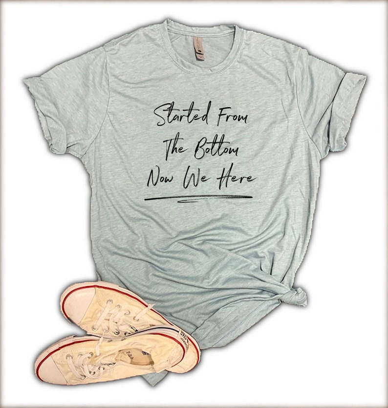 May include: A light blue t-shirt with the text "Started From The Bottom Now We Here" in black lettering.