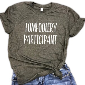 May include: A dark green t-shirt with the text "TOMFOOLERY PARTICIPANT" printed in white.