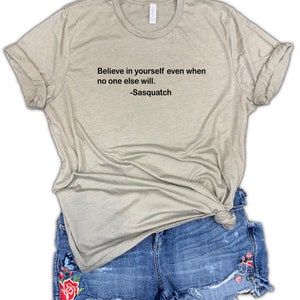 May include: A light beige t-shirt with the text "Believe in yourself even when no one else will. -Sasquatch" printed on the front.