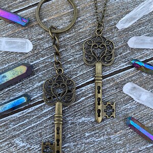 May include: Two antique-style skeleton keys, one on a chain and the other on a key ring. The keys are made of a brass-colored metal and have intricate designs.