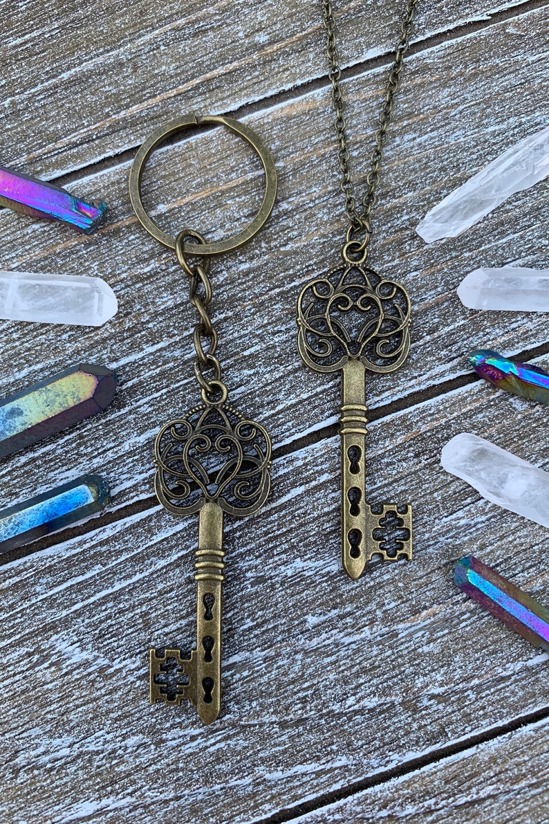 May include: Two antique-style skeleton keys, one on a chain and the other on a key ring. The keys are made of a brass-colored metal and have intricate designs.