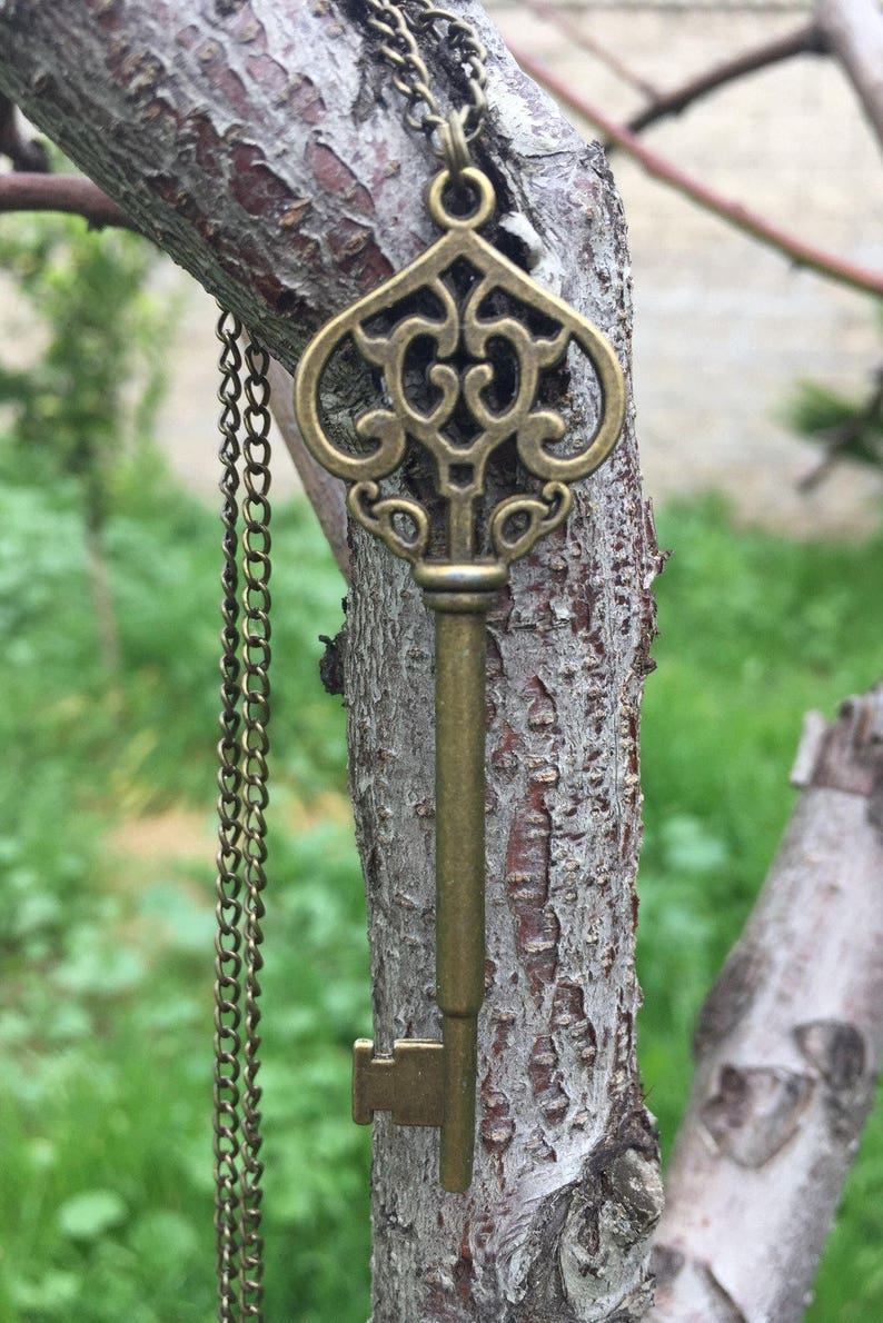 May include: A gold-toned key pendant necklace with an ornate design. The key is hanging from a chain on a tree branch.