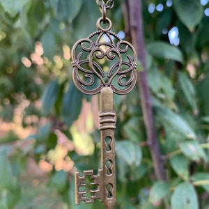 May include: A gold-toned key pendant necklace with a heart-shaped design and intricate details. The key is attached to a chain.