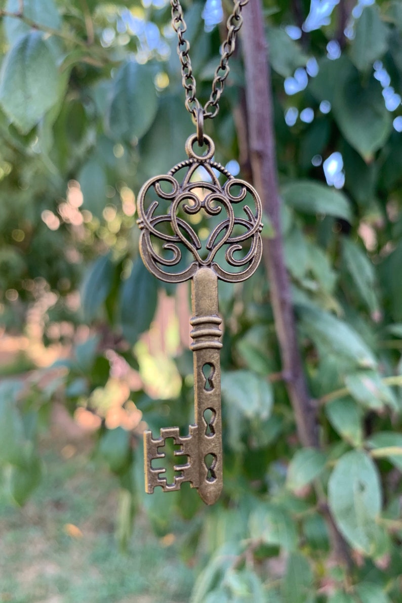 May include: A gold-toned key pendant necklace with a heart-shaped design and intricate details. The key is attached to a chain.