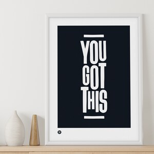 Puede incluir: Un p&oacute;ster motivacional en blanco y negro con el texto "YOU GOT THIS" en una fuente blanca en negrita. El p&oacute;ster est&aacute; enmarcado en un marco blanco y est&aacute; colgado en una pared blanca.