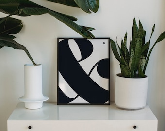 Puede incluir: Una impresión en blanco y negro del símbolo ampersand en un estilo gráfico audaz. La impresión está enmarcada en un marco negro y se muestra en una cómoda blanca con un jarrón y una planta en maceta.