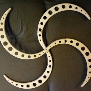 May include: A light-colored wooden decorative piece with a swirled design. The piece is composed of four curved segments, each with a series of evenly spaced circular holes. The design is symmetrical and appears to be handcrafted.