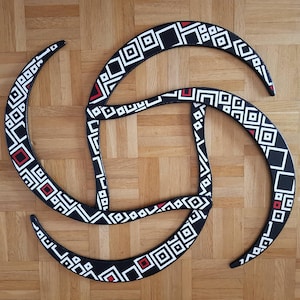 May include: Three black, white, and red geometric patterned wooden hoops, arranged in a circle, on a woodgrain surface.