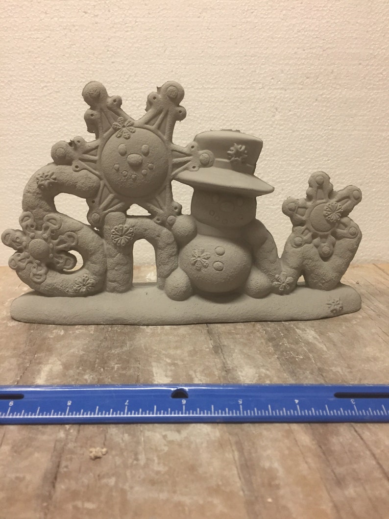 May include: A gray ceramic snowman figurine with a hat and a snowflake on top. The figurine is holding a snowflake in its right hand and the word "Snow" is spelled out in front of it.