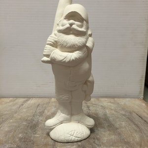 May include: White ceramic gnome figurine holding a baseball bat. The gnome is wearing a baseball cap and has a beard. The gnome is standing on a base that looks like a baseball.