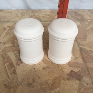 May include: Two white ceramic salt and pepper shakers with three holes on the top of each shaker.
