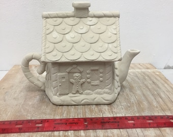 May include: A ceramic gingerbread house teapot, unpainted and ready for customization. The teapot features a chimney, a roof with textured shingles, and a handle shaped like a candy cane. A gingerbread man is embossed on the front.