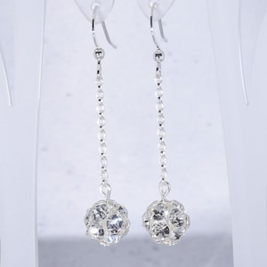 May include: Silver dangle earrings with a crystal ball charm at the end of each earring.