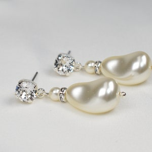 Può includere: Un paio di orecchini pendenti in argento con un cristallo trasparente e una grande perla barocca color avorio.