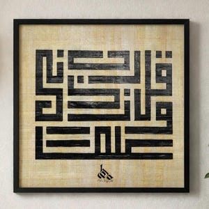 Puede incluir: Obra de arte enmarcada con caligrafía árabe negra sobre un fondo beige. La caligrafía está en un estilo geométrico audaz. El marco es negro y la obra de arte se exhibe en una pared de color claro. Una lámpara decorativa cuelga a la izquierda.