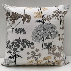 Peut inclure: Coussin carré avec un motif floral en nuances de gris, marron et jaune sur fond blanc. Le motif représente des fleurs sauvages. Le coussin a une finition texturée et une palette de couleurs neutres.