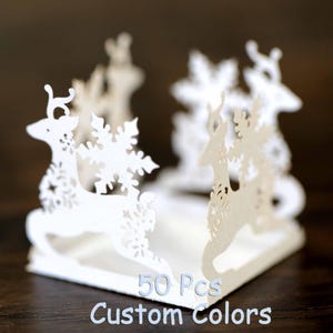 Könnte beinhalten: Weiße Papier-Rentier-Mittelstücke mit Schneeflocken-Designs. 50 Stück Kundenspezifische Farben.