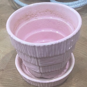 May include: A pink ceramic planter with a ribbed design and a matching saucer. The planter has a slightly faded appearance.