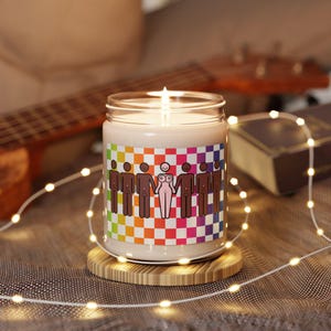 May include: A candle with a rainbow checkered pattern and a graphic of stick figures holding hands. The candle is on a wooden coaster.