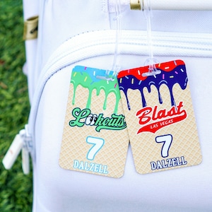 May include: Two luggage tags with a waffle cone design. One tag has green and blue dripping frosting with the text "Lookouts" and the number 7. The other tag has red and blue dripping frosting with the text "Blast Las Vegas" and the number 7. Both tags have the name "Dalzell".