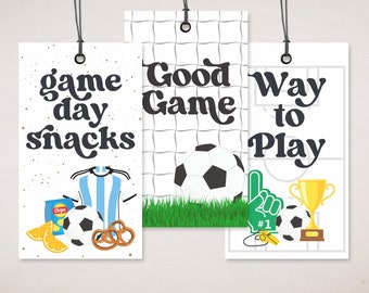 May include: Three printable tags with a soccer theme. The first tag says "game day snacks" and features a soccer ball, pretzels, chips, and oranges. The second tag says "Good Game" and features a soccer ball in front of a soccer net. The third tag says "Way to Play" and features a soccer ball, a trophy, a whistle, and a raised hand with a number one finger.