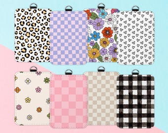 May include: A collection of rectangular cardholders with various patterns. Designs include leopard print, checkered patterns in lavender, pink, and tan, floral arrangements, a heart pattern, and a black and white buffalo check. Each has a silver ring.