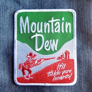 May include: Embroidered patch featuring the Mountain Dew logo with a green and white background. The patch includes a red figure aiming a rifle, with the text "It'll tickle yore innards!"