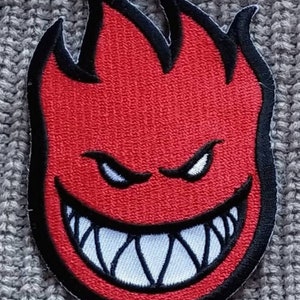 May include: Red and black embroidered patch with a flame design and a grinning face with sharp teeth.