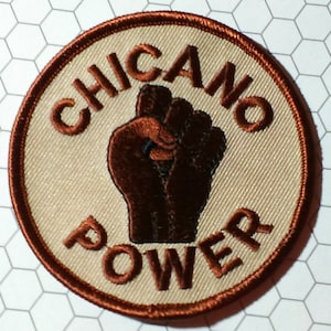 May include: A brown and beige embroidered patch with the text "CHICANO POWER" in brown lettering and a raised fist in the center.