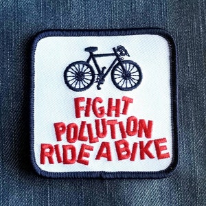 May include: White embroidered patch with a black bicycle silhouette and the text "FIGHT POLLUTION RIDE A BIKE" in red.