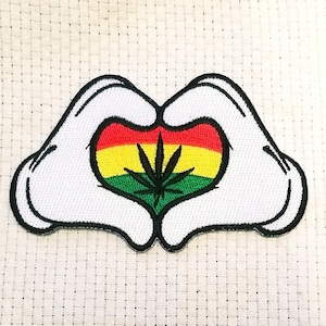 May include: White fabric patch with two hands forming a heart shape. Inside the heart is a green marijuana leaf with red, yellow, and green stripes.