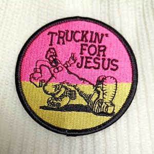 May include: A pink and gold embroidered patch with a cartoon figure and the text "Truckin' For Jesus".