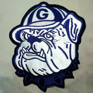 May include: A white bulldog wearing a blue baseball cap with a white "G" on it. The bulldog has a blue collar with spikes. The patch is embroidered.