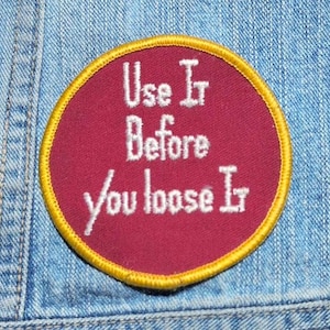 May include: A circular embroidered patch with a deep maroon background and a bright yellow stitched border. The patch features white embroidered text that reads Use It Before you loose It, centered in a clear, sans-serif font style.