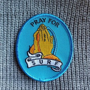 May include: A blue and yellow embroidered patch with the words "Pray for Surf" and a pair of hands clasped in prayer.