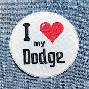 May include: A circular white embroidered patch featuring the black text I, the word my, and the word Dodge, with a red heart symbol replacing the word love. The patch has a white stitched border and is displayed on a blue denim fabric background.