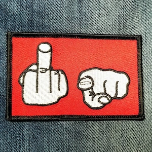 May include: A red patch with black stitching features two white embroidered hand gestures. The left hand is making a middle finger gesture, and the right hand is pointing directly at the viewer.