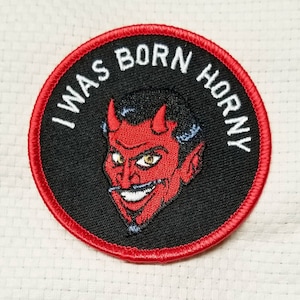 May include: A red and black embroidered patch with a cartoon devil and the text "I WAS BORN HORNY".