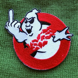 May include: Embroidered patch featuring a white ghost with sunglasses giving the middle finger, inside a red circle with a black outline. The ghost is partially obscured by red and black shards.