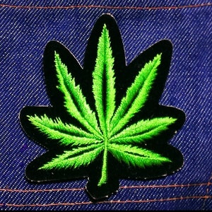 May include: Green marijuana leaf embroidered patch on a blue denim background.