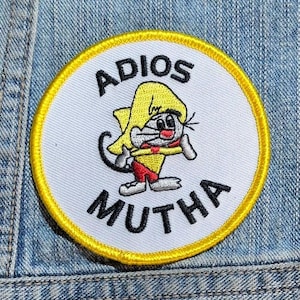 May include: A circular embroidered patch with a white background and a yellow border. It features a cartoon character wearing a yellow sombrero and red shorts, with the black text ADIOS above and MUTHA below the character in a bold font.