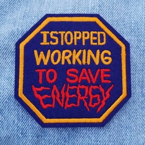 May include: A blue and yellow octagonal patch with the text "I STOPPED WORKING TO SAVE ENERGY" in red and yellow embroidery.