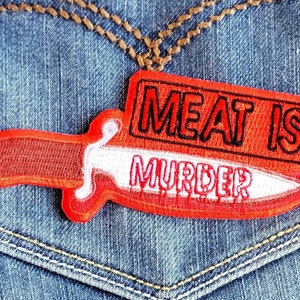 May include: Red and white embroidered patch with a knife shape and the text "Meat is Murder".